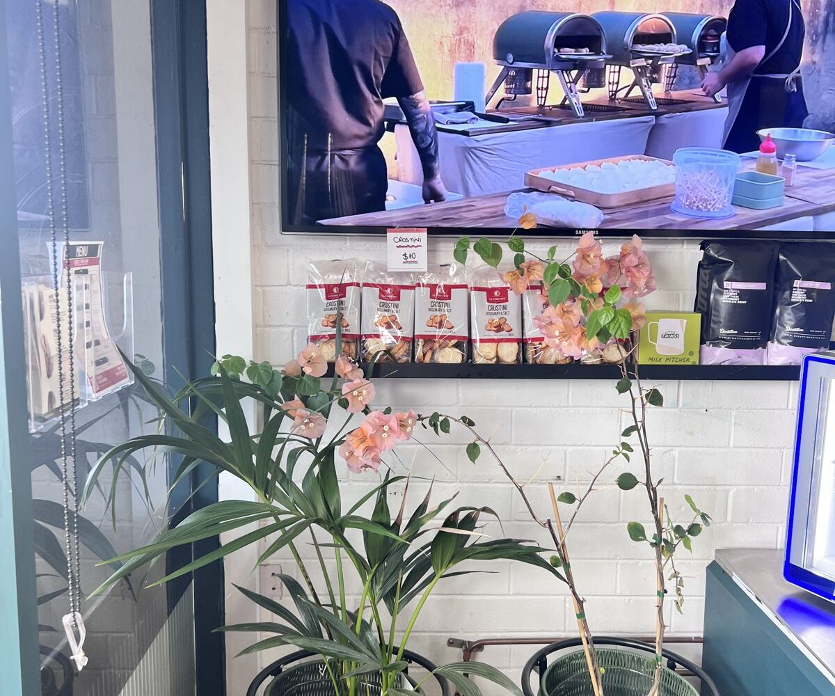 Wall-mounted display shelf beneath the TV screen near the entrance and takeaway ordering area of an Italian cafe in Balcatta, Perth